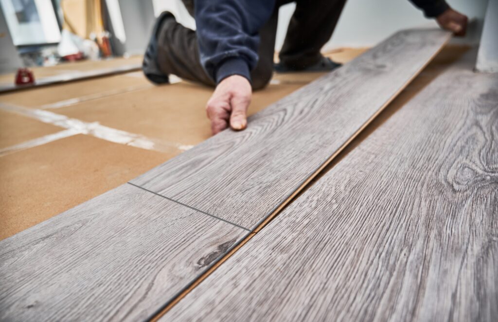 Male worker hands laying laminate flooring in apartment.